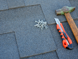 Various types of Carlsbad roofing tools including a hammer, box cutter, and roofing shingle nails.